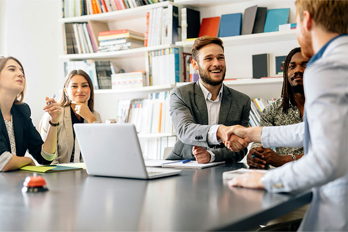Group of young professionals in a meeting, one man shaking hands, representing cool kids who peaked in high school now.