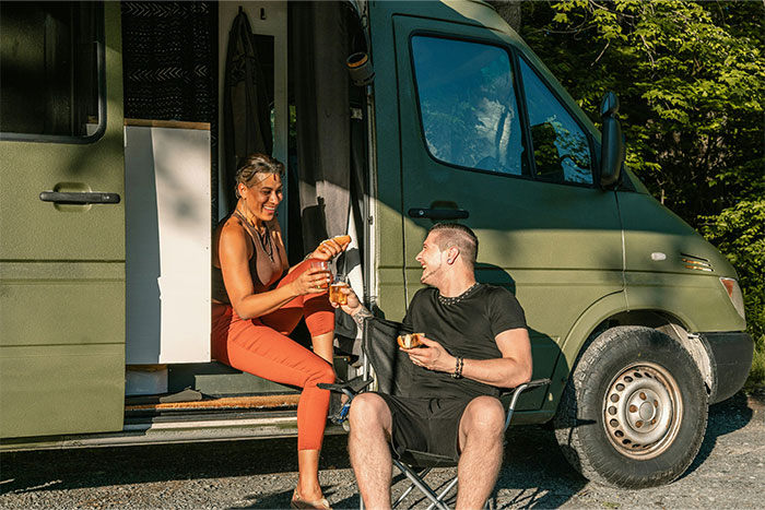 Two friends enjoying snacks and drinks by a green camper van, reflecting what cool kids who peaked in high school do now