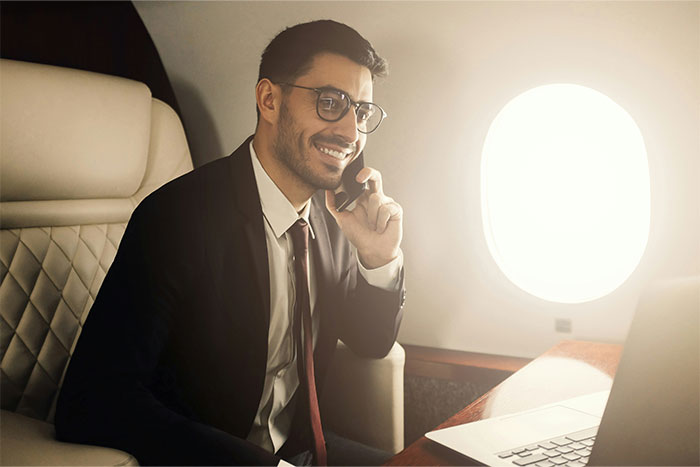 Man smiling and talking on phone in private jet cabin, illustrating what cool kids who peaked in high school are doing now
