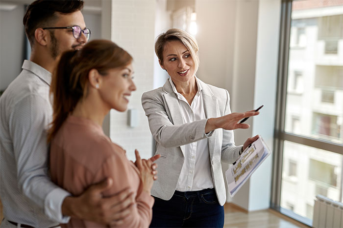 A woman showing a couple around a modern apartment, illustrating what cool kids who peaked in high school are doing now.