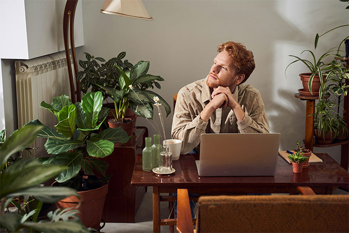 Young man working on a laptop surrounded by plants, reflecting on what the cool kids who peaked in high school are doing now.