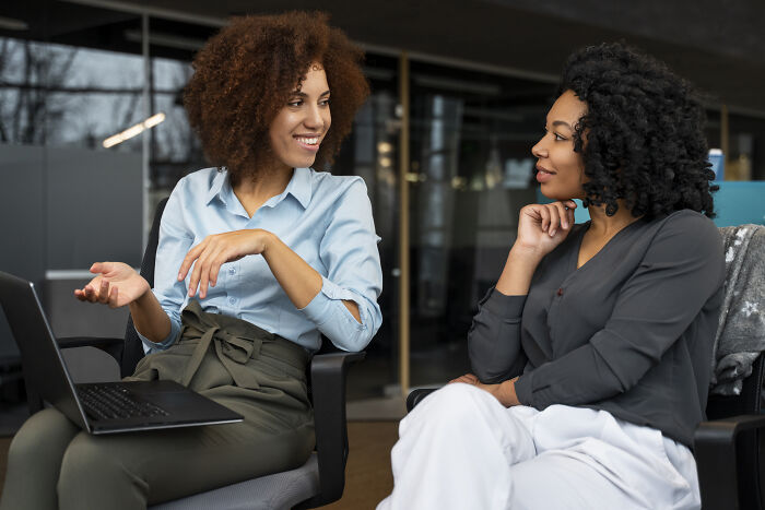 Two professional women having a conversation in an office setting, demonstrating how to call out corporate pals’ lies.