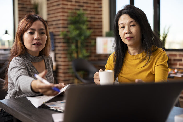 Two corporate colleagues discussing work in an office, one pointing at a laptop, focusing on calling out lies.