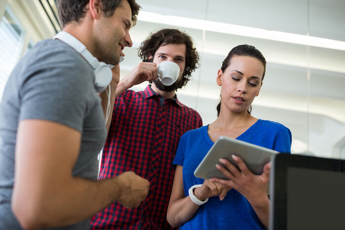 Three corporate colleagues in a casual office setting discussing work while one looks at a tablet, illustrating calling out lies.
