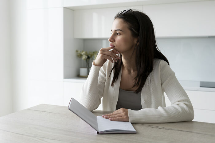 Young woman in a white sweater sitting at a table with an open notebook, contemplating how to call out corporate pals’ lies.