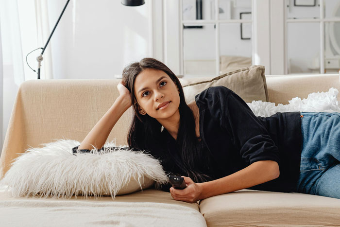 Young woman lying on a sofa holding a remote, representing a non-fandom cosplay party experience. Young woman lying on a sofa holding a remote, representing a non-fandom cosplay party experience.