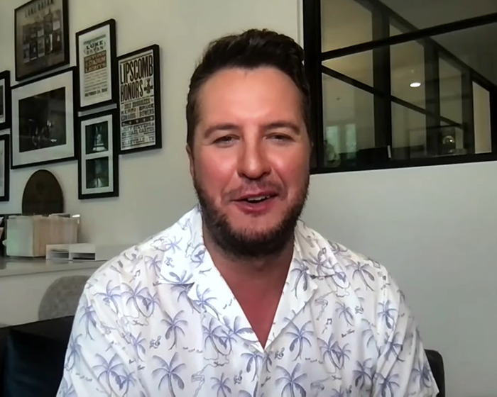Country star wearing a white patterned shirt, smiling during an indoor interview about abruptly stopping mid-concert.