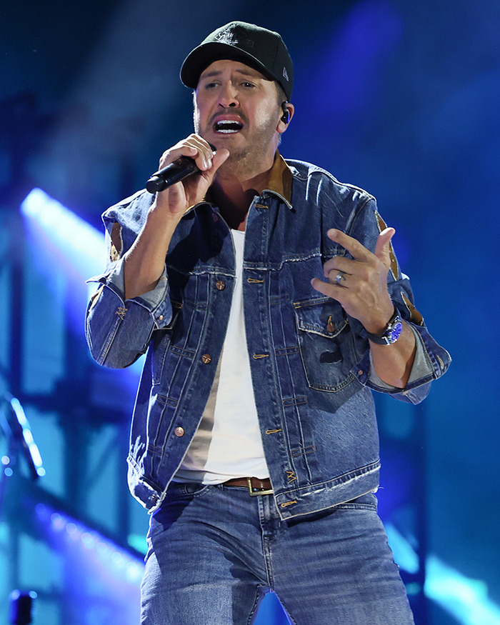 Country star performing on stage wearing denim jacket and cap during a concert with intense facial expression.