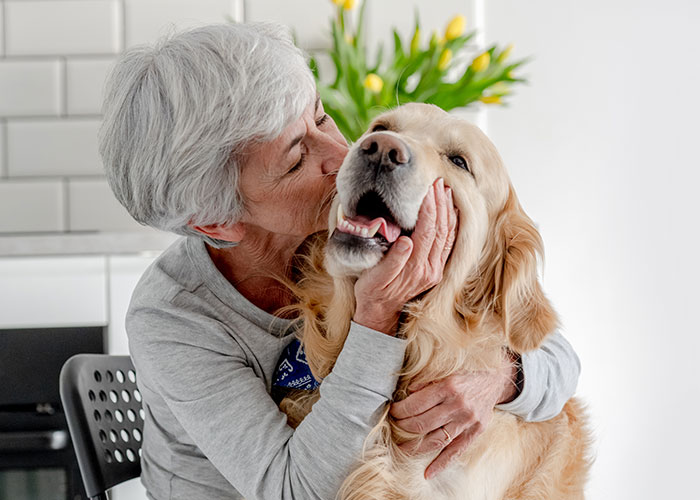 Older woman affectionately hugging a golden retriever indoors, highlighting a woman&rsquo;s garden landscaped without permission.