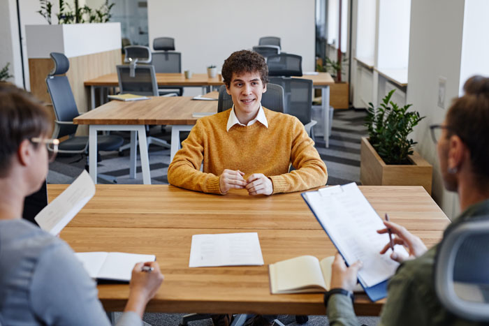 Young man in a mustard sweater at a job interview, discussing employment opportunities in a modern office setting.