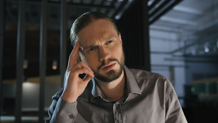 Man in gray shirt thoughtfully touching temple, reflecting on a job cousin finds through a friend conversation.