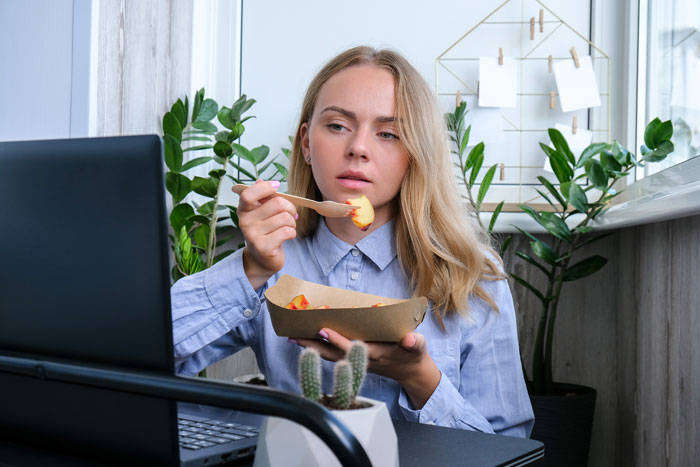 Woman eating lunch at her desk, illustrating workers adding labels to protect food from lunch thieves.
