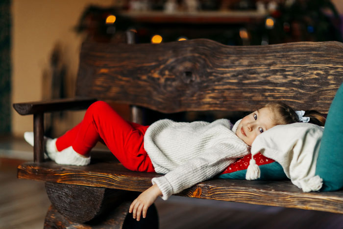 Child lying on wooden bench indoors, wearing warm clothes, depicting a cold night and troubled family situation. Child lying on wooden bench indoors, wearing warm clothes, depicting a cold night and troubled family situation.
