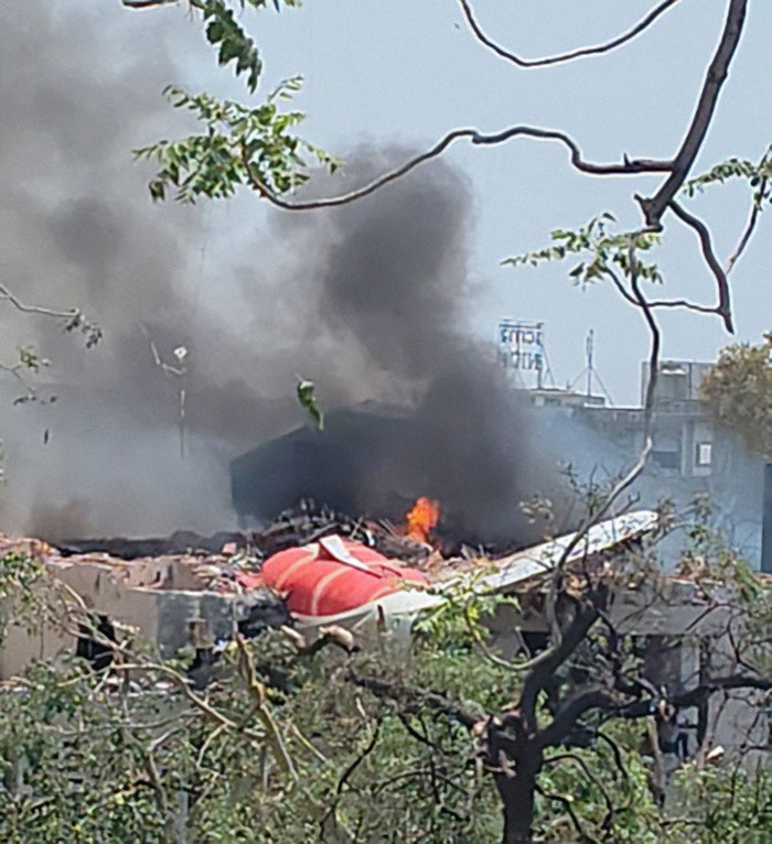 Smoke and flames rising from the wreckage of an Air India plane crash site near buildings and trees.