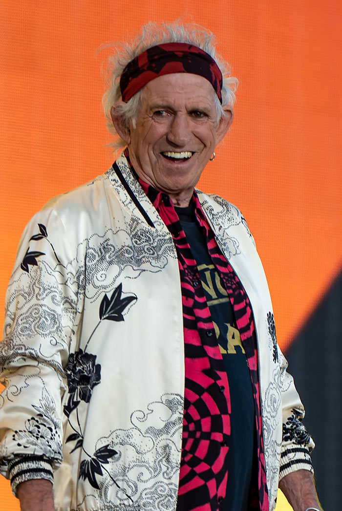 Older male celebrity wearing a patterned white jacket and headband, smiling on stage amid wildest celebrity rumors discussion.
