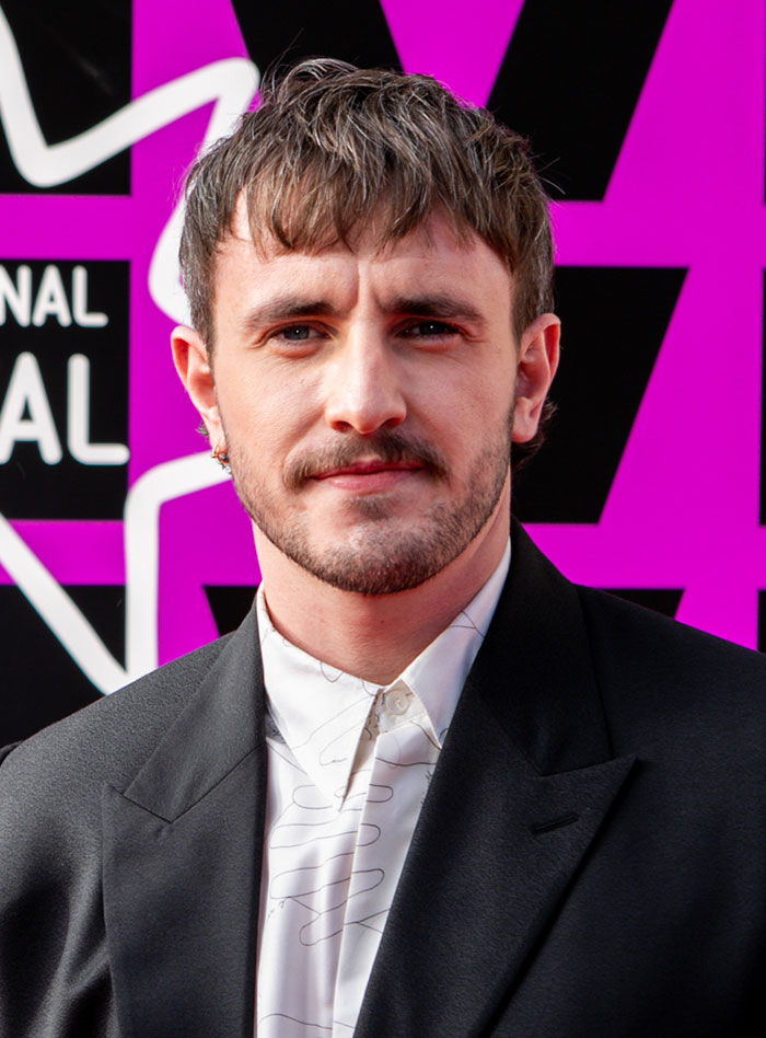 Young man in a black blazer and patterned white shirt posing at an event about wild rumors going around about celebrities