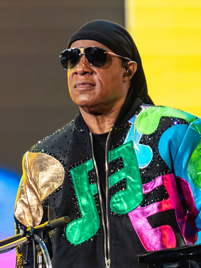 A celebrity musician wearing sunglasses and a colorful jacket performing on stage amid wild celebrity rumors.