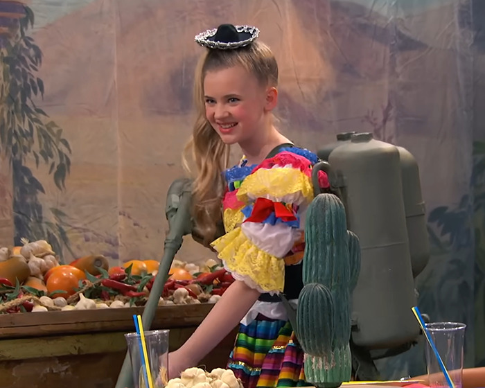 Child star in colorful costume with a backpack device, smiling amid a festive setting highlighting unrecognizable transformation concerns.