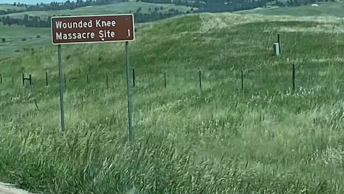 Road sign for Wounded Knee M******e Site in a grassy field, one of the creepy and chilling spots in the U.S.