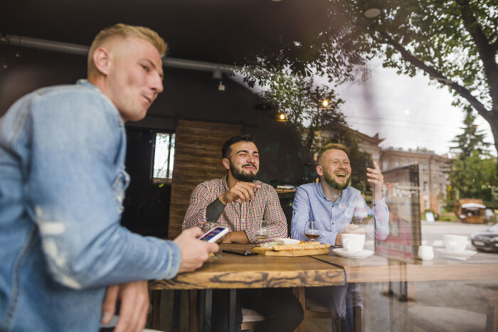 Three men laughing and enjoying drinks inside a cozy café near creepy and chilling spots in the U.S.