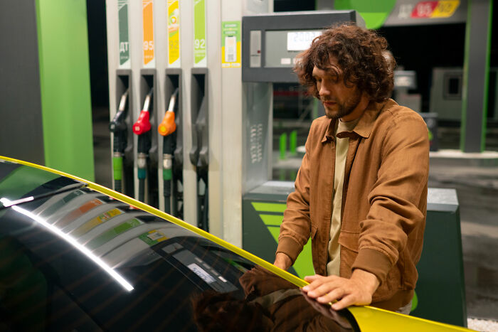Man with curly hair standing beside a car at a gas station, evoking a chilling spot from creepy places in the U.S.