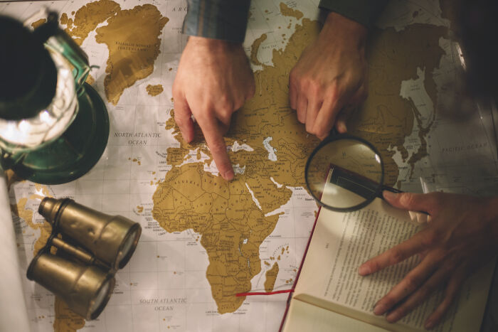 Hands pointing on a world map and reading a book with a magnifying glass exploring things people thought everyone knew