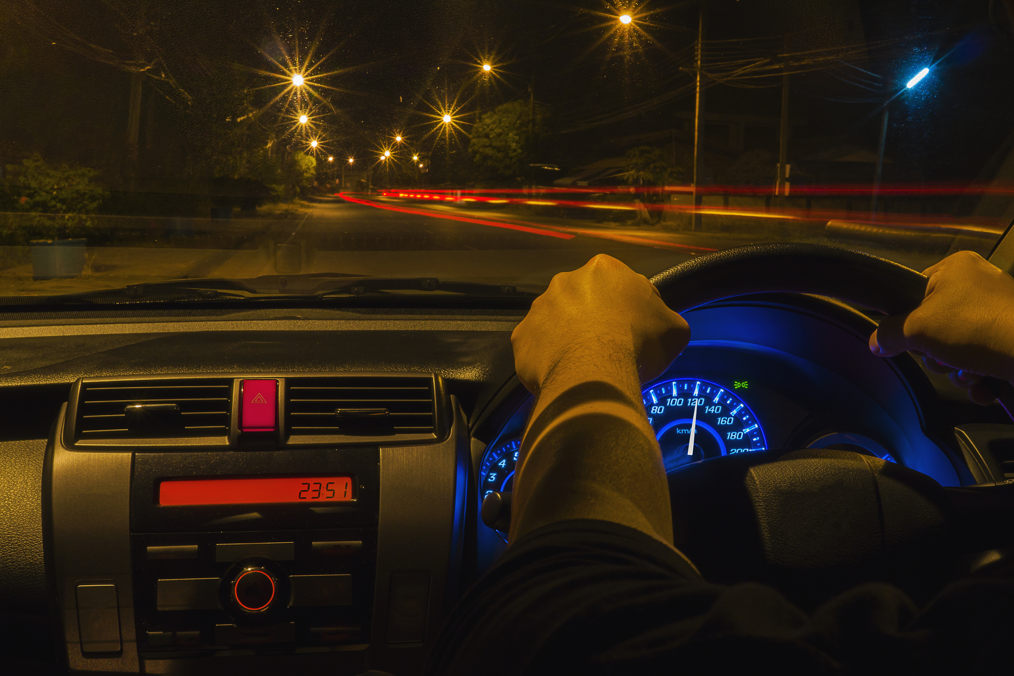 Driver holding the steering wheel at night with illuminated speedometer and street lights on dark road showing safe driving facts
