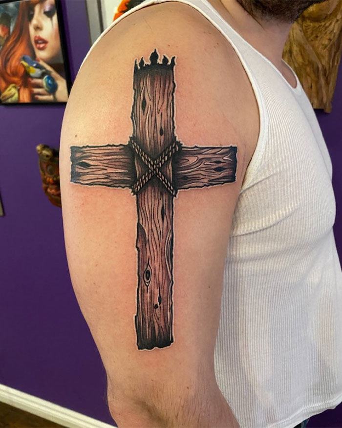 Arm tattoo of a wooden cross with rope details, showcasing a detailed cross tattoo design for men.