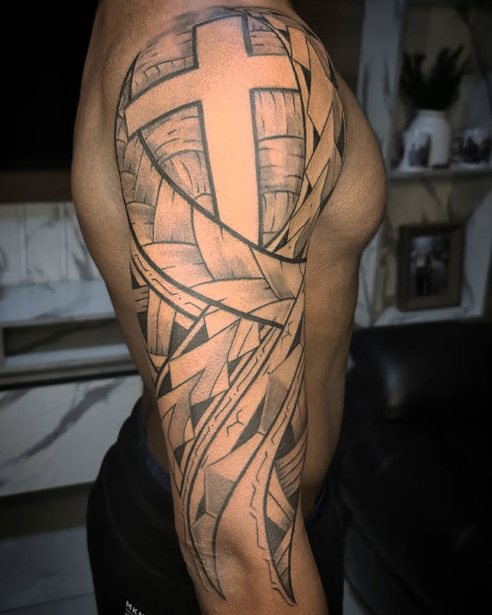 Intricate cross tattoo on a man&rsquo;s upper arm featuring geometric and abstract black ink designs.
