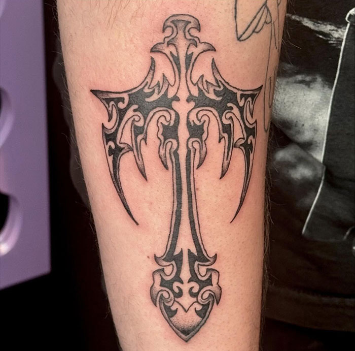 Black and gray cross tattoo with tribal design on forearm showcasing visual guide to cross tattoos for men.