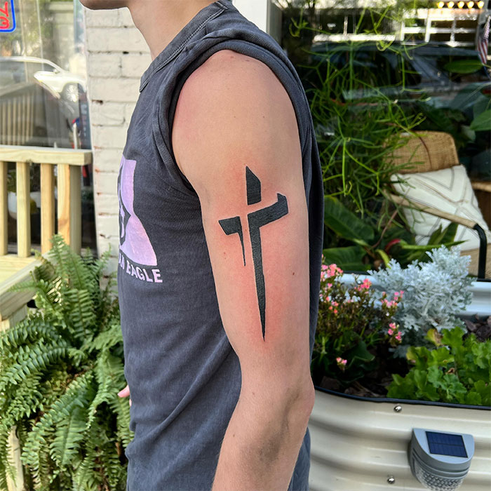 Man with a bold black cross tattoo on upper arm, showcasing a unique design in a casual outdoor setting for cross tattoos men.