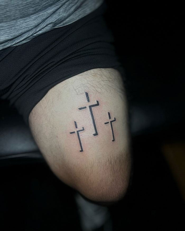 Minimalist black cross tattoos on a man's thigh featuring three simple and clean cross designs.