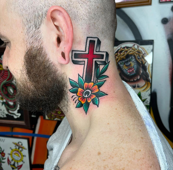 Man with colorful cross tattoo behind ear featuring a flower and leaves, showcasing stylish cross tattoos for men.