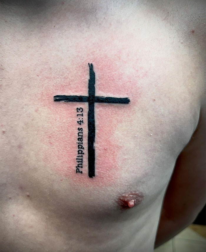 Black cross tattoo with Philippians 4:13 text inked on a man's upper chest, showcasing cross tattoos for men.