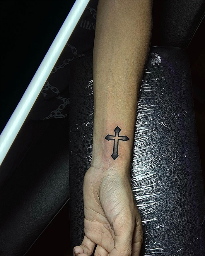 Black cross tattoo on the inner wrist of a man, showcasing bold outline and shading in a visual guide to cross tattoos.