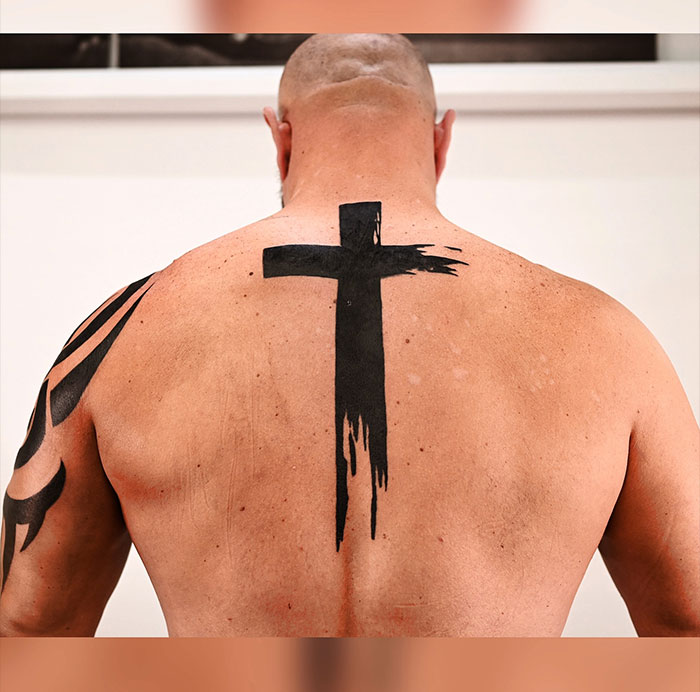 Man with a bold black cross tattoo on his upper back, showcasing a unique design in cross tattoos for men.