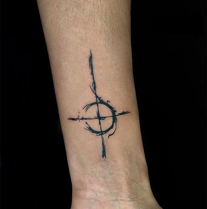 Abstract black cross tattoo on a man's forearm with artistic brushstroke design, showcasing unique cross tattoos for men.