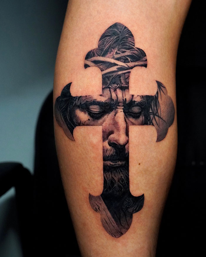Black ink cross tattoo on a man's arm featuring a detailed realistic face inside the cross design.
