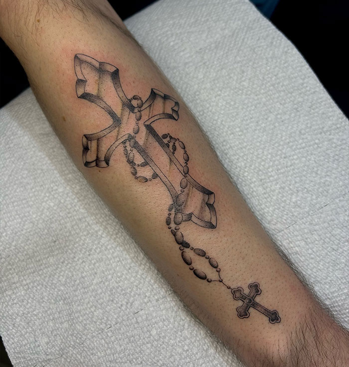 Cross tattoos for men on forearm featuring a large 3D cross and a smaller cross on a rosary beaded chain.