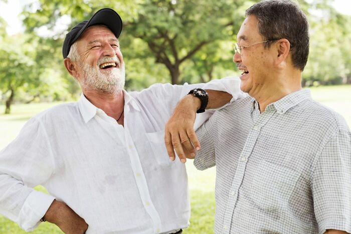 Two men laughing together outdoors smiling and chatting, private resort worker sharing insights in a casual setting