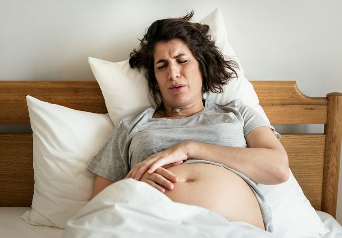 Pregnant woman in gray shirt lying in bed, experiencing discomfort during childbirth and postpartum recovery.