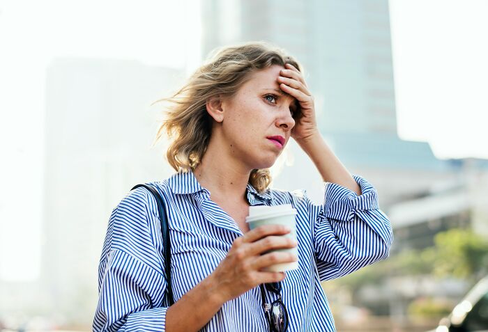 Stressed woman outdoors holding a coffee cup, appearing overwhelmed, illustrating feelings related to postpartum OCD.