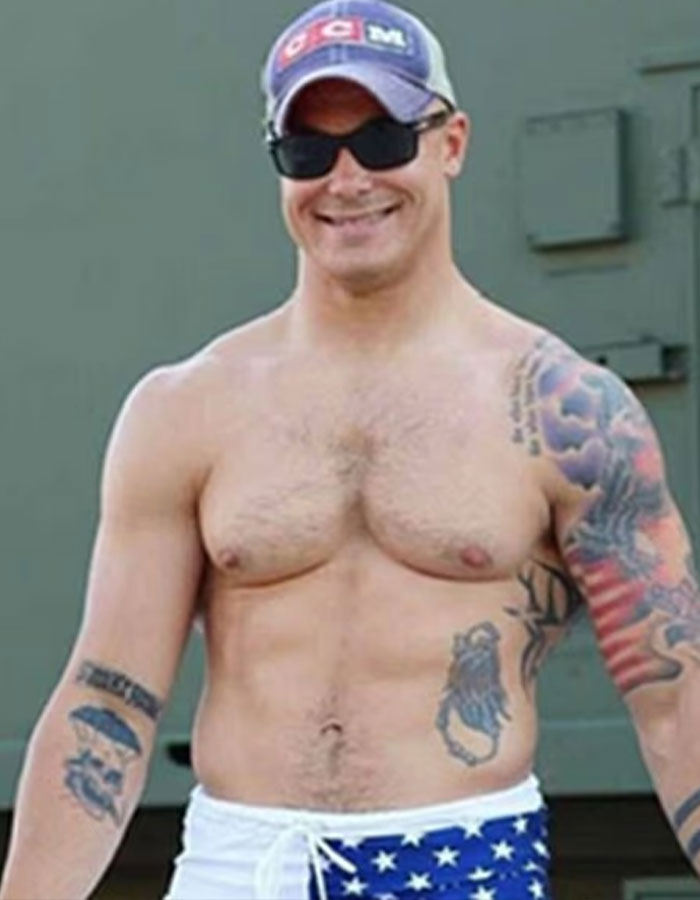 Shirtless man wearing sunglasses and a cap, showing tattoos, related to police search and likely hideout keywords.