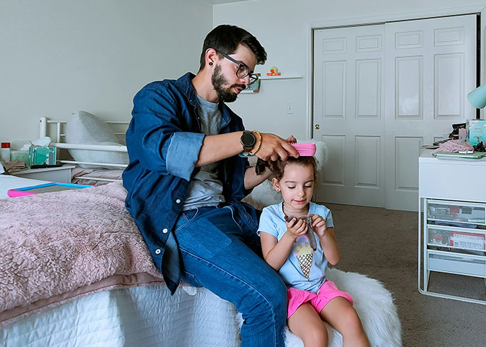 Father brushing young daughter's hair at home, illustrating parents discovering kids were not biologically theirs experience.