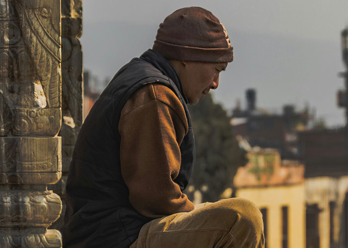 Man wearing a beanie and vest sitting alone outdoors, appearing deep in thought about parents finding out kids weren’t biological.