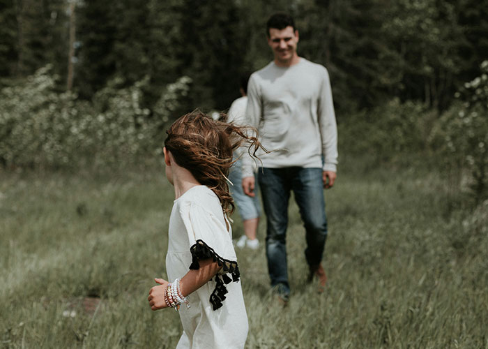 Parents discovering their children are not biologically theirs, walking in a grassy outdoor setting with trees in background.