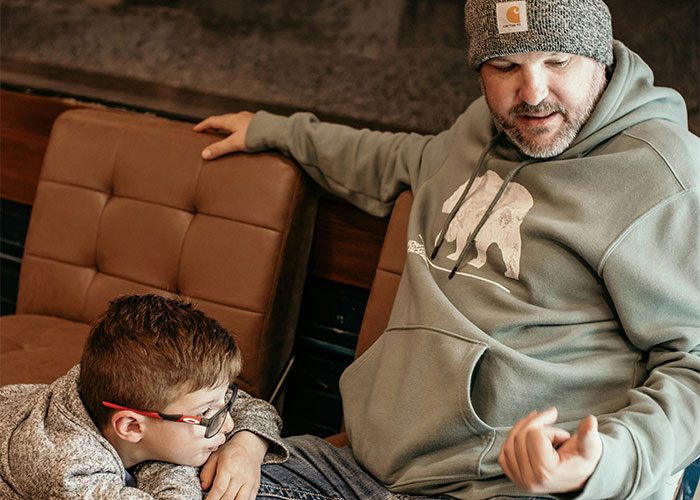Father and son sitting on a couch, sharing a serious moment about discovering children are not biologically theirs.
