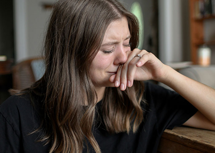 Woman with long brown hair sitting indoors, crying quietly while covering her mouth, depicting parents' heartbreak discovering kids not biological.