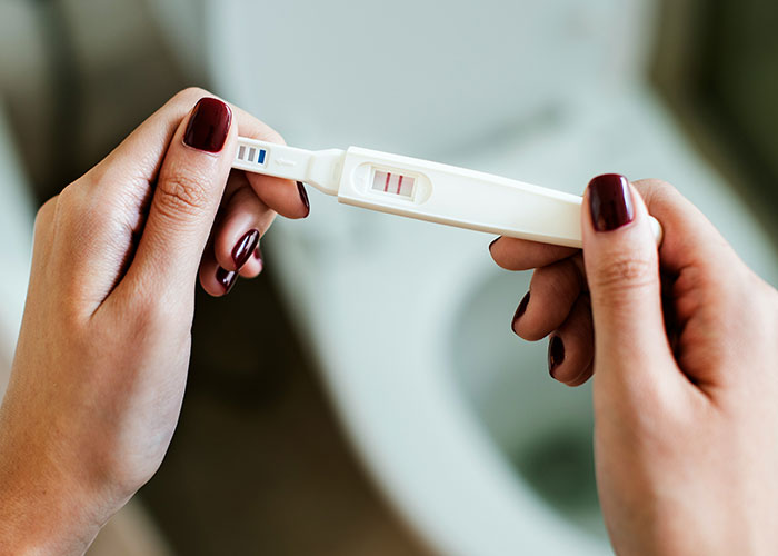 Hands with dark red nail polish holding a positive pregnancy test, symbolizing parents discovering kids aren’t biologically theirs.