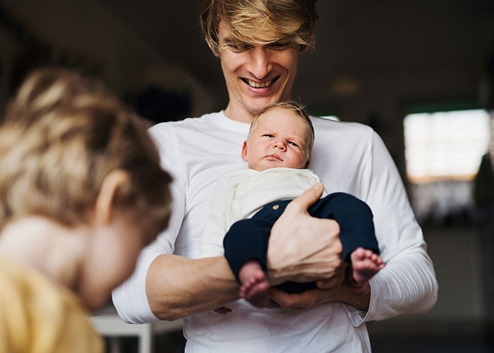 Father holding baby with older child in foreground, representing parents discovering kids aren’t biologically theirs.